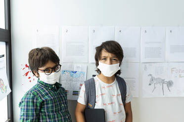 Schoolboys wearing masks standing against wall in school - VABF02998
