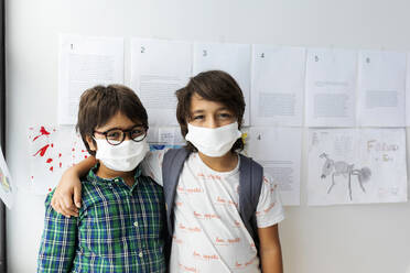 Friends wearing masks standing against wall in school - VABF02999