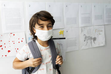 Junge mit Maske steht gegen Papiere an der Wand in der Schule - VABF03001