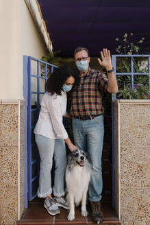 Man wearing mask waving hand while woman looking at dog - AGGF00084