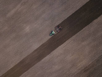 Russland, Oblast Moskau, Luftaufnahme eines Traktors, der ein braunes Feld pflügt - KNTF04661