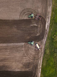 Russia, Moscow Oblast, Aerial view of two tractors plowing brown field - KNTF04662