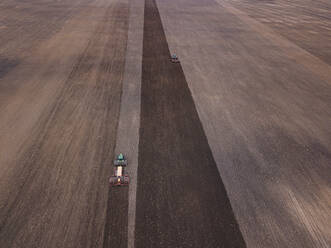 Russia, Moscow Oblast, Aerial view of two tractors plowing vast brown field - KNTF04663