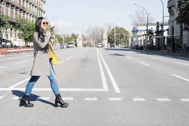 Stylish young woman talking over smart phone while crossing road in city - JCZF00130