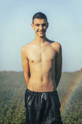 Shirtless teenage boy enjoying sprinkler in farm against clear sky - ACPF00736