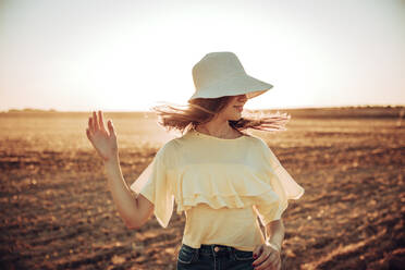 Young woman tossing hair on field against sky during sunset - ACPF00743