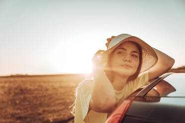 Nachdenkliche junge Frau lehnt an Auto auf Feld gegen klaren Himmel bei Sonnenuntergang - ACPF00746