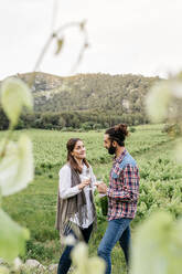 Glückliches Paar mit Weingläsern in der Hand im Gespräch auf einem Weinberg - JRFF04494