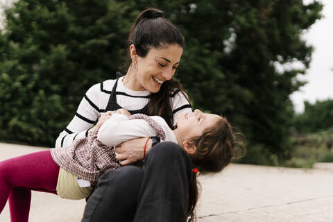 Playful mother and daughter on street during sunny day stock photo