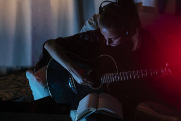 Female musician playing guitar on sofa in recording studio at home - ERRF03962