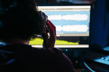 Man holding headphones while using computer in recording studio at home - ERRF03971