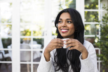 Thoughtful young woman smiling while holding coffee cup at cafe - ABZF03166