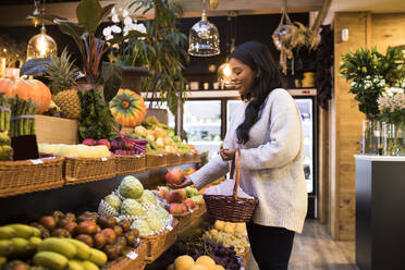 Junge Frau trägt Weidenkorb beim Kauf von Obst im Lebensmittelgeschäft - ABZF03176