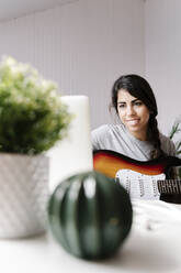 Glückliche junge Frau, die einen Laptop benutzt, während sie mit einer E-Gitarre zu Hause sitzt - JMHMF00052