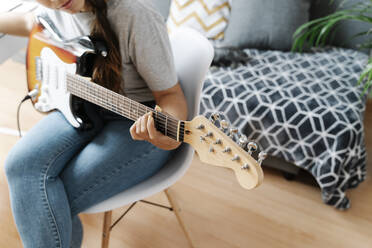 Frau spielt E-Gitarre, während sie auf einem Stuhl zu Hause sitzt - JMHMF00056