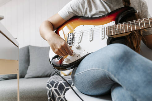 Woman adjusting knobs on electric guitar at home - JMHMF00057