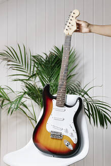 Cropped image of woman's hand holding electric guitar on chair at home - JMHMF00072