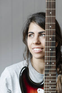 Thoughtful young woman with electric guitar against wall at home - JMHMF00076