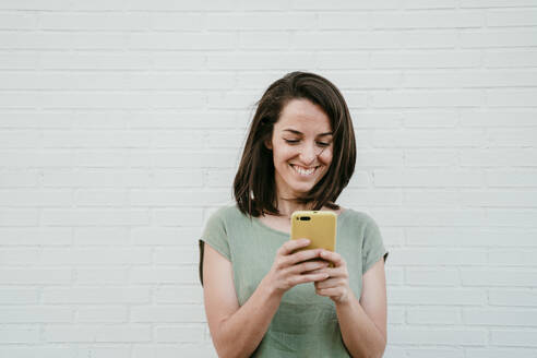 Porträt einer glücklichen Frau, die auf ihr Handy schaut - EBBF00172