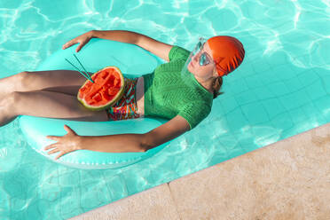 Woman with floating tire and watermelon in swimming pool - ERRF03973