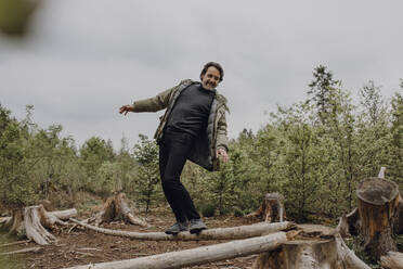 Mature hiker balancing on tree trunk in the forest - JLOF00430