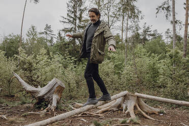 Älterer Wanderer balanciert auf einem Baumstamm im Wald - JLOF00431