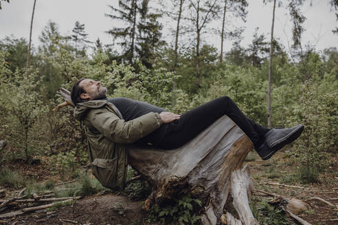 Älterer Wanderer auf einem Baumstumpf im Wald liegend - JLOF00432