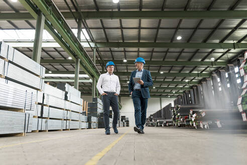 Two businessmen having a meeting and walking in a factory - MOEF02903