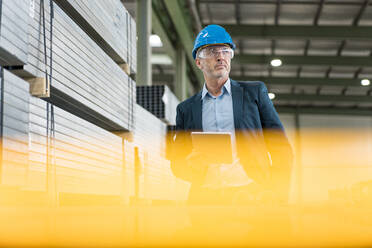 Älterer Geschäftsmann mit Tablet trägt Schutzhelm und Schutzbrille in einer Fabrik - MOEF02907