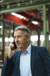 Porträt eines reifen Geschäftsmannes am Telefon in einer Fabrik - MOEF02913