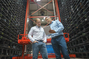 Two businessmen with tablet in a high rack warehouse of a factory - MOEF02929