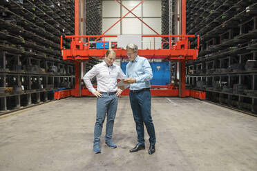 Two businessmen with tablet in a high rack warehouse of a factory - MOEF02931