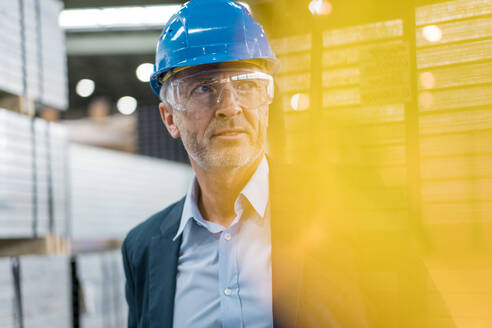 Portrait of mature businessman wearing hard hat and safety goggles in a factory - MOEF02941