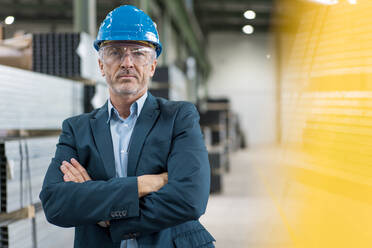 Portrait of mature businessman wearing hard hat and safety goggles in a factory - MOEF02943