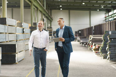 Two businessmen having a meeting and walking in a factory - MOEF02954