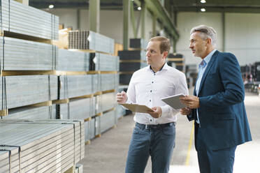Two businessmen with tablet and clipboard having a meeting in a factory - MOEF02955