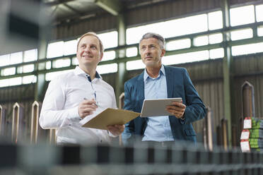 Two businessmen with tablet and clipboard having a meeting in a factory - MOEF02957