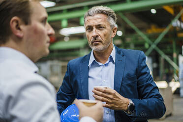 Zwei Geschäftsleute mit Kaffee bei einer Besprechung in einer Fabrik - MOEF02958