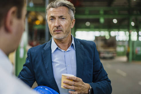 Zwei Geschäftsleute mit Kaffee bei einer Besprechung in einer Fabrik - MOEF02961