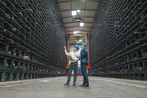 Two businessmen having a meeting in a high rack warehouse of a factory - MOEF02966