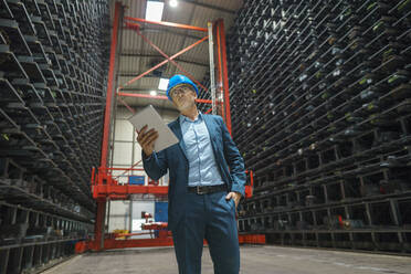 Mature businessman using tablet in a high rack warehouse of a factory - MOEF02973