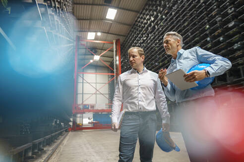 Two businessmen having a meeting in a high rack warehouse of a factory - MOEF02983