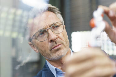 Portrait of mature businessman examining industrial product - MOEF02991