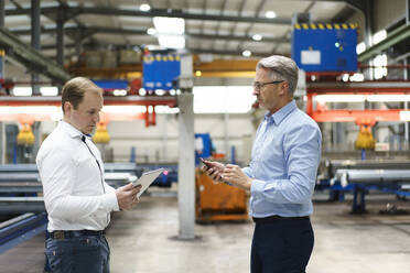 Zwei Geschäftsleute mit Tablet und Mobiltelefon bei einem Treffen in einer Fabrik - MOEF03005
