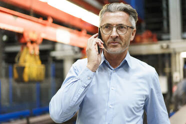 Porträt eines reifen Geschäftsmannes am Telefon in einer Fabrik - MOEF03006