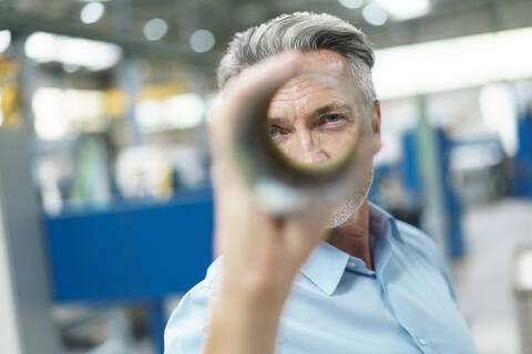 Geschäftsmann hält Stahlrohr in einer Fabrik, lizenzfreies Stockfoto