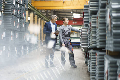 Businessman and worker talking in a factory storehouse - MOEF03031