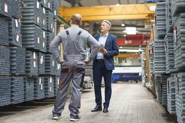 Businessman and worker talking in a factory storehouse - MOEF03032