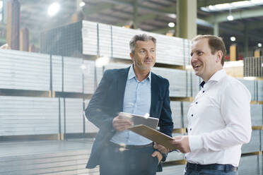 Businessman with tablet and happy employee with clipboard in a factory - MOEF03057