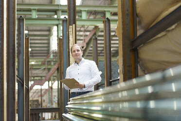 Businessman with clipboard at steel pipes in a factory - MOEF03063